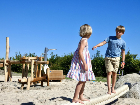 Dos niños juegan descalzos sobre una cuerda en la arena en Zonneweelde Lodge XL en los Países Bajos.
