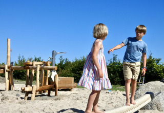 Dos niños juegan descalzos sobre una cuerda en la arena en Zonneweelde Lodge XL en los Países Bajos.