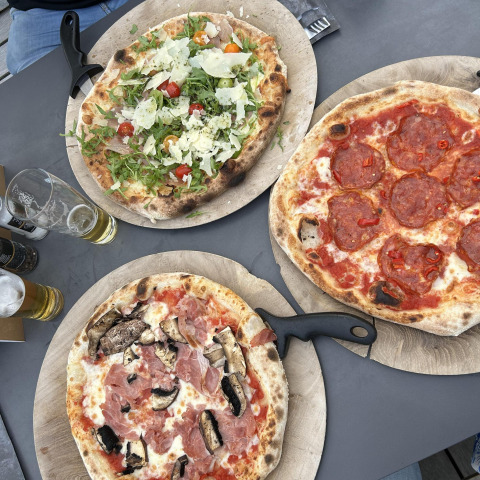 Tres pizzas variadas sobre tablas de madera con cerveza, servidas en una mesa dentro de un lodge moderno.