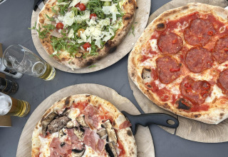 Tres pizzas variadas sobre tablas de madera con cerveza, servidas en una mesa dentro de un lodge moderno.