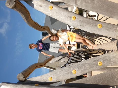 Two kids playing on a wooden playground structure at Zonneweelde Lodge XL, Camping Zonneweelde, Netherlands.