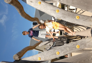 Two kids playing on a wooden playground structure at Zonneweelde Lodge XL, Camping Zonneweelde, Netherlands.