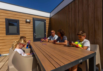 Famiglia gioca a carte all'aperto presso Zonneweelde Lodge XL al Camping Zonneweelde nei Paesi Bassi.