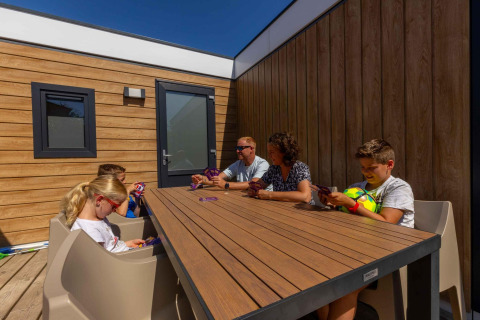 Familie nyder kortspil udendørs ved Zonneweelde Lodge XL på Camping Zonneweelde i Holland.