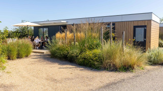 Moderne Zonneweelde Lodge bij Camping Zonneweelde, Nederland, mensen genieten buiten onder parasol.