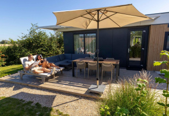 Due persone si rilassano sulla terrazza di Zonneweelde Lodge al Camping Zonneweelde nei Paesi Bassi, sotto un ombrellone.