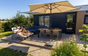 Dos personas relajándose en la terraza de Zonneweelde Lodge en Camping Zonneweelde, Países Bajos, bajo una sombrilla.