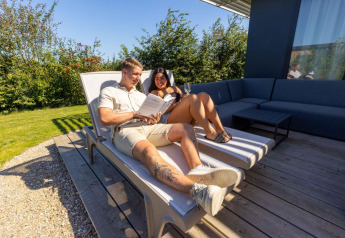 Couple relaxing on lounge chairs at Zonneweelde Lodge, Camping Zonneweelde in the Netherlands, enjoying sunshine.