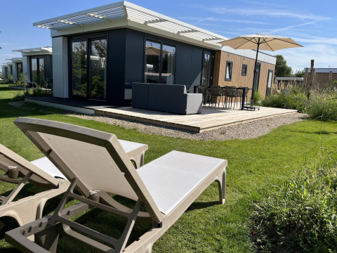 Outdoor terrace with sun loungers and umbrella at Zonneweelde Lodge, Camping Zonneweelde, Netherlands.