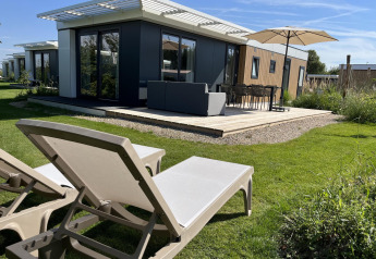 Outdoor terrace with sun loungers and umbrella at Zonneweelde Lodge, Camping Zonneweelde, Netherlands.