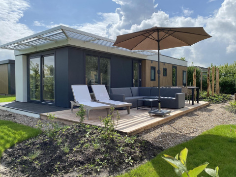 Moderne lodge met zonneterras, ligbedden, parasol en loungeset bij Camping Zonneweelde in Nederland.