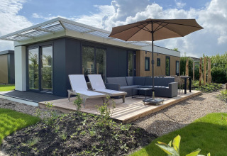 Moderna cabaña con terraza, tumbonas, sombrilla y sofá en Camping Zonneweelde, Países Bajos, a pleno sol.