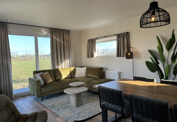 Modern living room in Zonneweelde Lodge at Camping Zonneweelde, Netherlands, with green sofa and dining table.