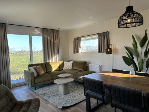 Moderne stue i Zonneweelde Lodge, Camping Zonneweelde, Holland med stort vindue, grøn sofa og spisebord.