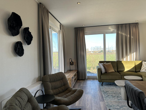 Moderne woonkamer in Zonneweelde Lodge, Camping Zonneweelde, Nederland, met grote ramen en stijlvolle inrichting.
