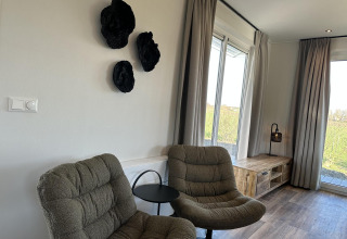 Moderne zithoek in Zonneweelde Lodge met twee comfortabele stoelen, zwarte wanddecoratie en ruime ramen.