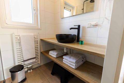 Baño moderno con lavabo negro, estantes de madera, toallas limpias y ventana en Zonneweelde Lodge, Países Bajos.