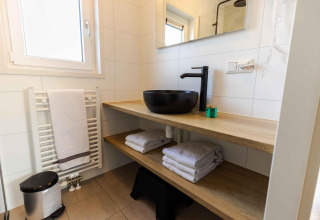 Baño moderno con lavabo negro, estantes de madera, toallas limpias y ventana en Zonneweelde Lodge, Países Bajos.