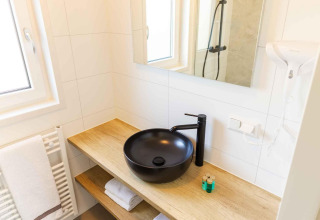 Modern badkamer in Zonneweelde Lodge met zwarte waskom, houten blad, spiegel en witte handdoeken.