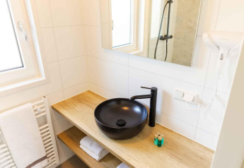 Salle de bain moderne à la Zonneweelde Lodge avec vasque noire, plan en bois, miroir et serviettes blanches.