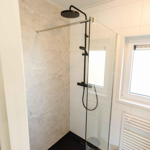 Moderne douche met zwarte kraan en glazen wand in Zonneweelde Lodge op Camping Zonneweelde, Nederland.