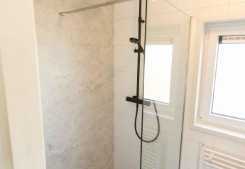 Doccia moderna con rubinetteria nera e divisorio in vetro nella Zonneweelde Lodge al Camping Zonneweelde, Paesi Bassi.