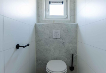 Moderno baño blanco con inodoro suspendido, pequeña ventana y cubo en Zonneweelde Lodge, Países Bajos.