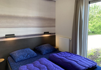 Bedroom in Zonneweelde Lodge at Camping Zonneweelde, Netherlands, with two beds, purple duvets and garden view.