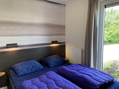 Dormitorio en Zonneweelde Lodge en Camping Zonneweelde, Países Bajos, con dos camas, edredones y vista al jardín.