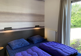 Dormitorio en Zonneweelde Lodge en Camping Zonneweelde, Países Bajos, con dos camas, edredones y vista al jardín.