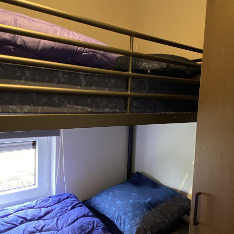 Literas con ropa de cama azul y morada en Zonneweelde Lodge, Camping Zonneweelde, Países Bajos.