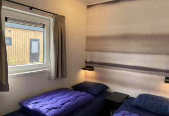Chambre moderne avec deux lits simples et couettes violettes, vue sur la façade bois, Zonneweelde Lodge.