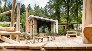 Speeltuin met houten structuren voor moderne lodges bij Resort Veluwe, Silva, Nederland, omgeven door bos.