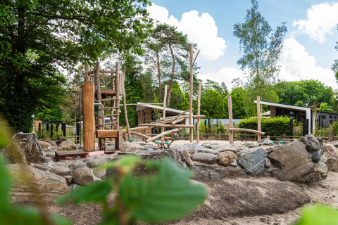 Buitenspeeltuin bij Silva Lodge met houten speeltoestellen, stenen en omgeven door groen landschap.