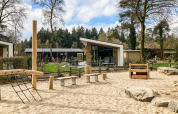 Legeplads med træudstyr og sand foran moderne hytter ved Silva Playground, Resort Veluwe, Holland.