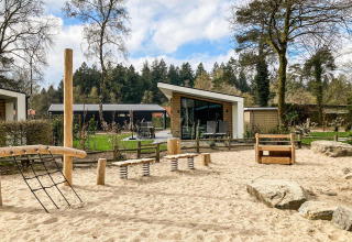 Parque infantil con equipo de madera y arena frente a cabañas modernas en Silva Playground, Resort Veluwe, Países Bajos.