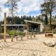 Parco giochi con attrezzature in legno e sabbia davanti a lodge moderni a Silva Playground, Resort Veluwe, Paesi Bassi.