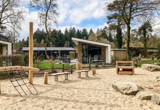 Speelplein met houten speeltoestellen en zand voor moderne lodges bij Silva Playground, Resort Veluwe, Nederland.