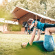 Una persona juega con un niño en el césped frente a una tienda safari Vecht Glamping Lodge rodeada de naturaleza.