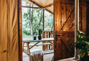 Vista da una tenda safari alla Vecht Glamping Lodge, Beerze Bulten, con arredi in legno e molto verde.