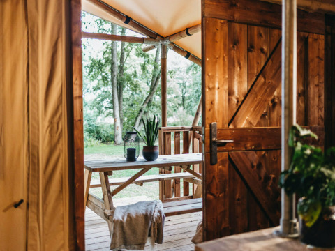 Vista da una tenda safari alla Vecht Glamping Lodge, Beerze Bulten, con arredi in legno e molto verde.