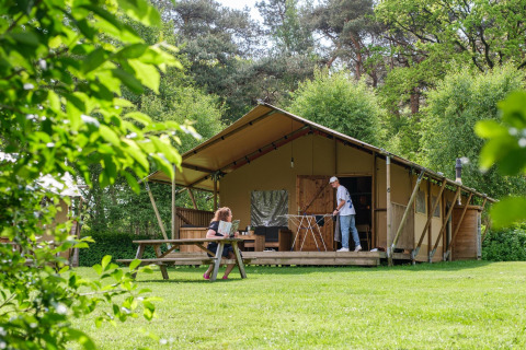 To personer nyder udendørs aktiviteter foran et safari-telt kaldet Vecht Glamping Lodge i Beerze Bulten.