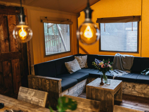 Hyggelig opholdsstue i Vecht Glamping Lodge, Beerze Bulten, med træmøbler og varme belysning.