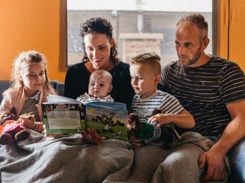 Familia sentada junta leyendo un libro en una tienda safari en Vecht Glamping Lodge, Beerze Bulten, Países Bajos.