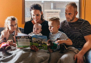 Familia sentada junta leyendo un libro en una tienda safari en Vecht Glamping Lodge, Beerze Bulten, Países Bajos.