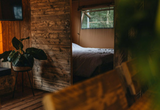 Indvendigt billede af en hyggelig safari telt lodge med trævægge, planter og et soveområde ved Beerze Bulten.
