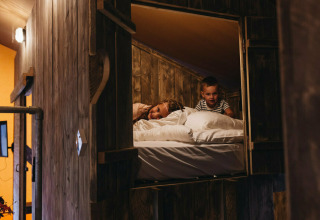 Dos niños se relajan en una cama elevada en Vecht Glamping Lodge, Beerze Bulten, Países Bajos.