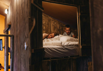 Two children relax in a cozy loft bed at Vecht Glamping Lodge, Beerze Bulten, the Netherlands.