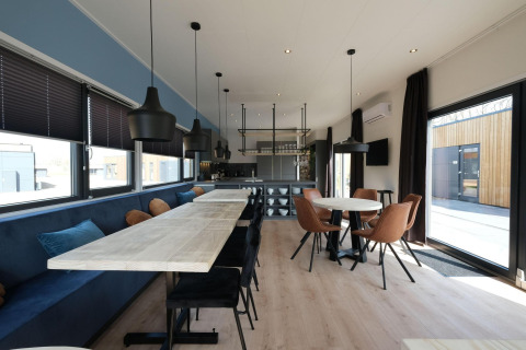 Modern dining area with long wooden tables and round table at Amalia Familia lodge, Hofparken Wiltershaar, Netherlands.