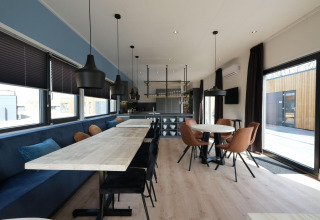Zona pranzo moderna con tavoli in legno al lodge Amalia Familia presso Hofparken Wiltershaar, Paesi Bassi.